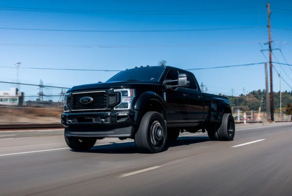 A black Ford F-450 dually pickup truck driving down a road on a clear sunny day with the background blurred by motion.