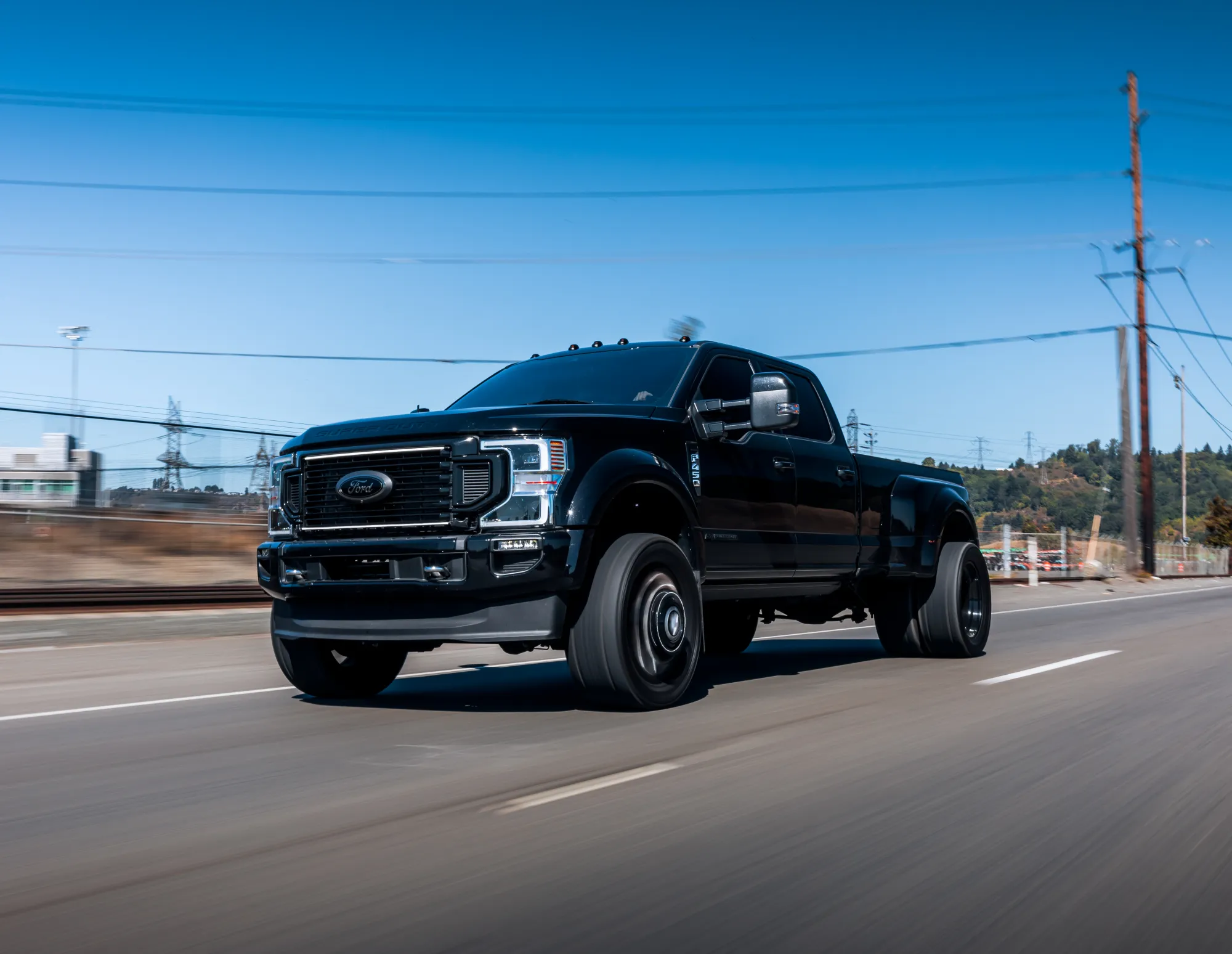 A black Ford F-450 dually pickup truck driving down a road on a clear sunny day with the background blurred by motion.